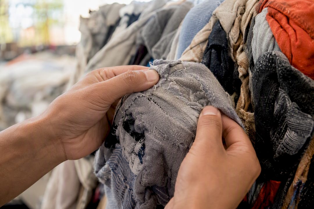 Hands inspecting fabric of used clothing bale